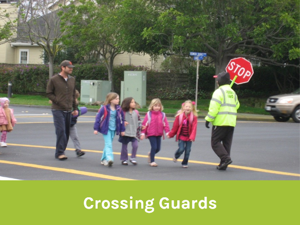 Image of a parent and children walking past a crossing guard at an intersection.