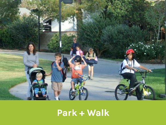 Image of children and parents biking and walking down a path through a park area.