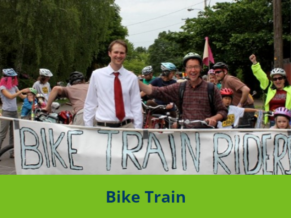 Image of two adults holding a "Bike Train Riders" poster with children and parents behind them.