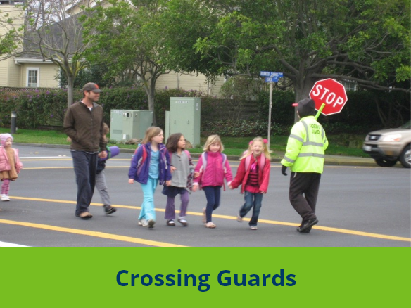 Image of a parent and children walking past a crossing guard at an intersection.