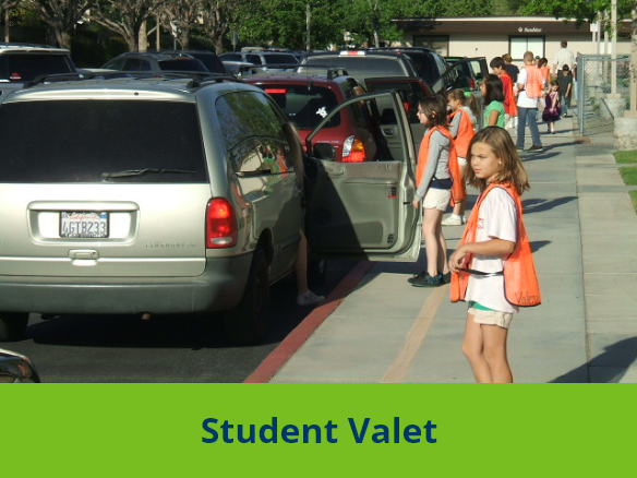 Image of students on the sidewalk wearing orange vests holding doors open for cars while students step out of the cards.